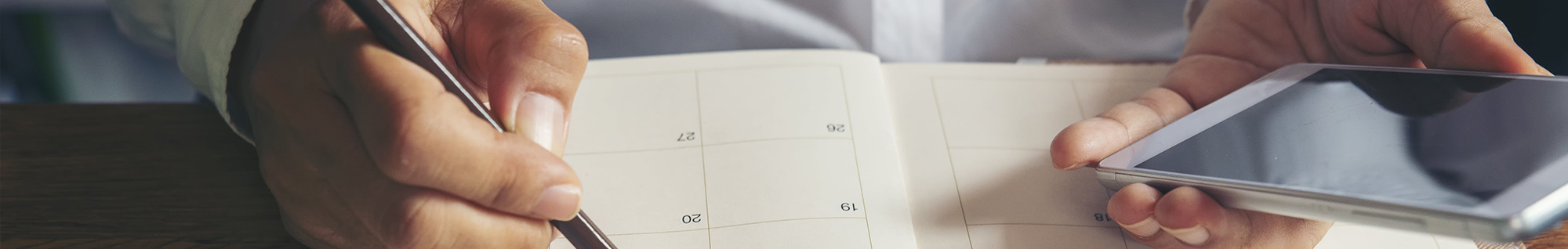 Parent writing notes in her calendar while looking at her phone