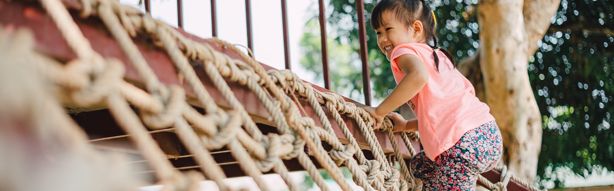 Happy little girl climbing a jungle gym rope